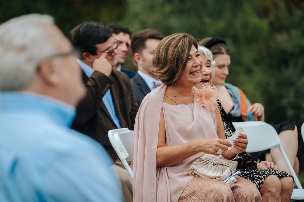 Wedding guests laugh and celebrate while drinking from wine glasses during an outdoor reception celebration.