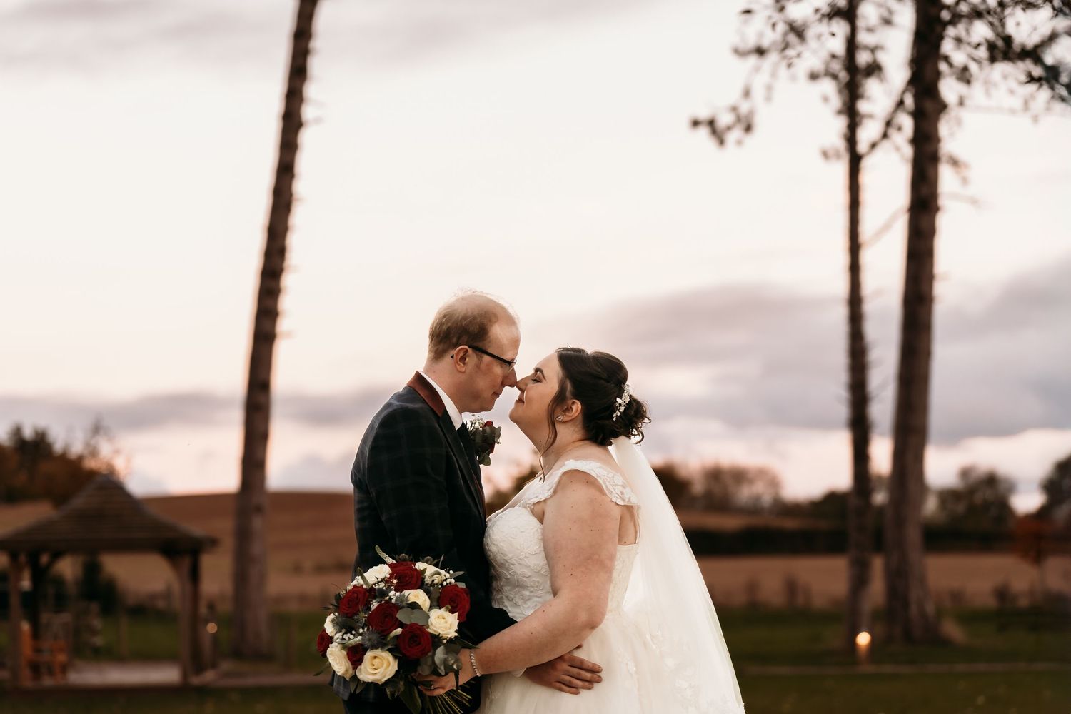 A romantic kiss at sunset outdoors near tall pine trees with moody clouds in the background.