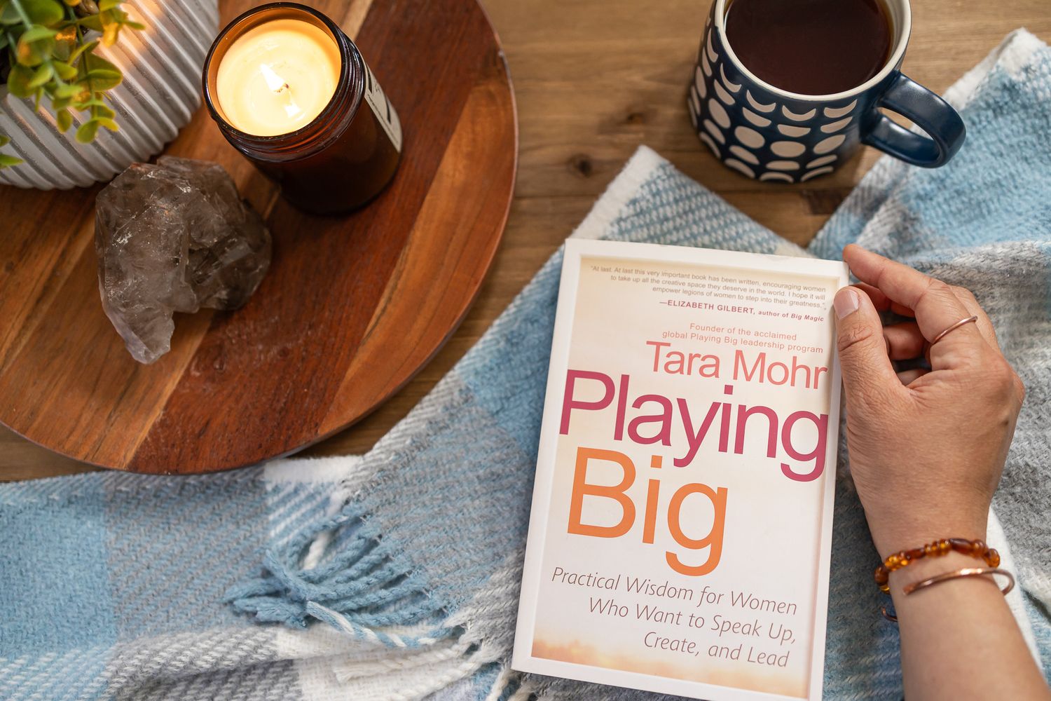 staged flat lay overhead book Playing Big by Tara Mohr on blanket with hand, candle, plant, crystal and cup of tea on table in Seattle, WA