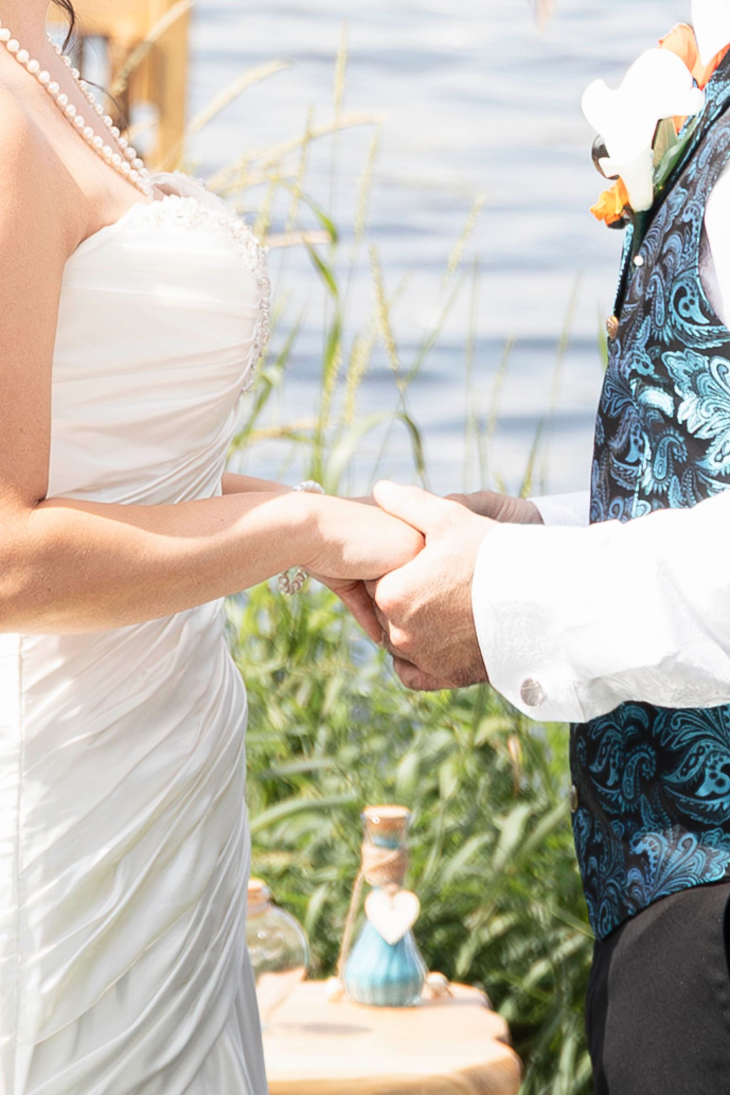 Close-up of bride and groom holding hands during outdoor wedding ceremony.