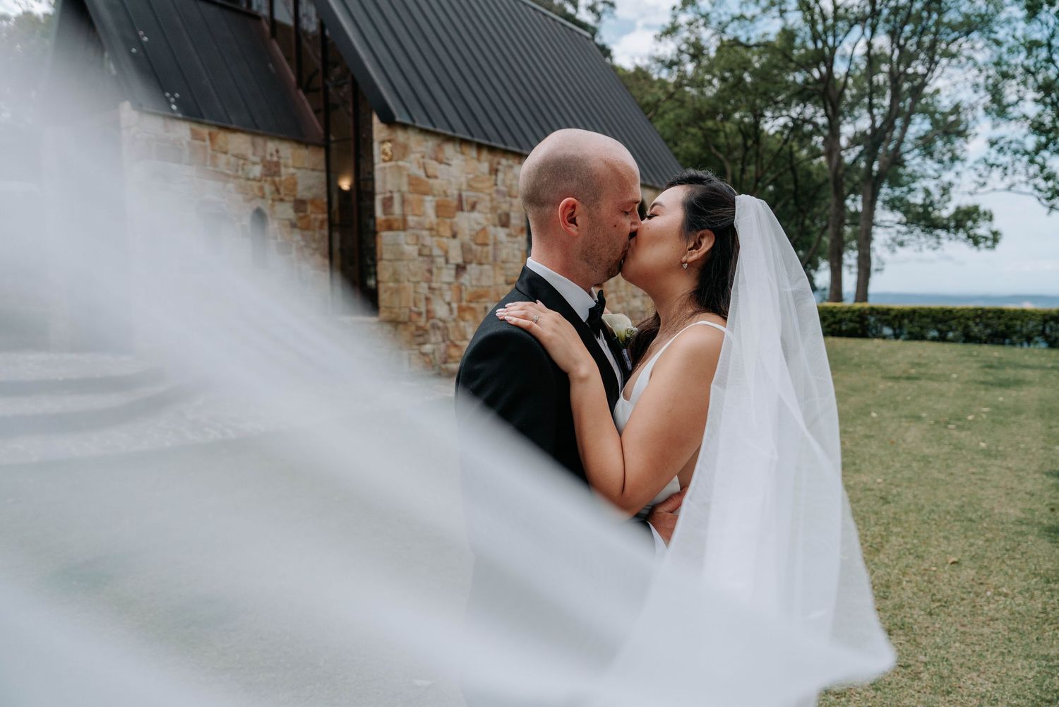Wedding ceremony taking place in a window-lined venue with views of willow trees and a lake.