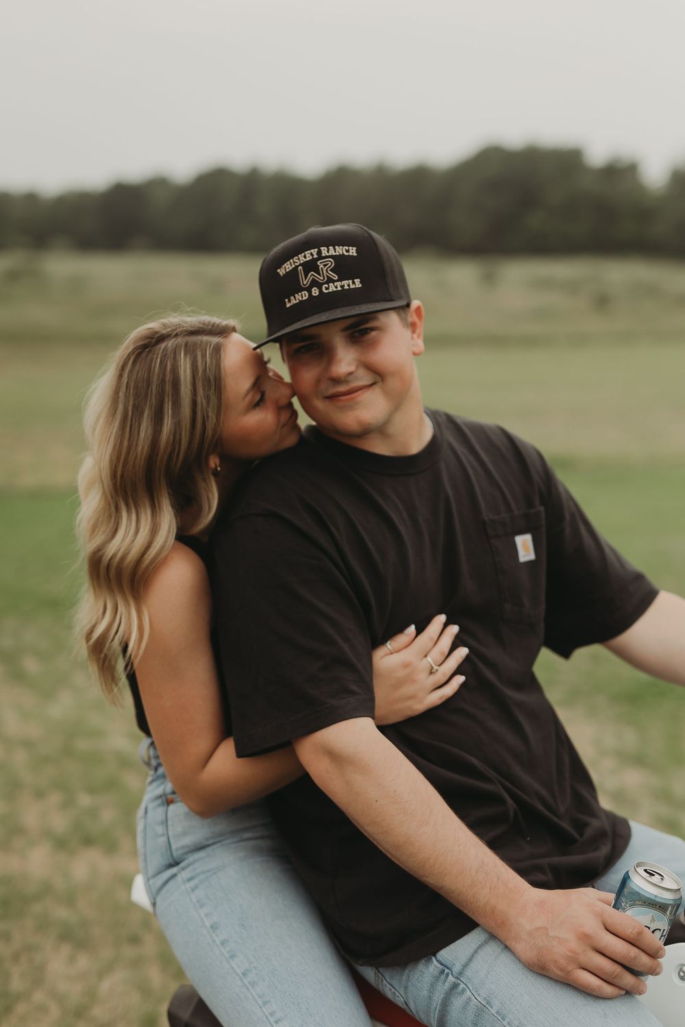 A couple embraces while sitting on a motorcycle in a grassy field during golden hour.