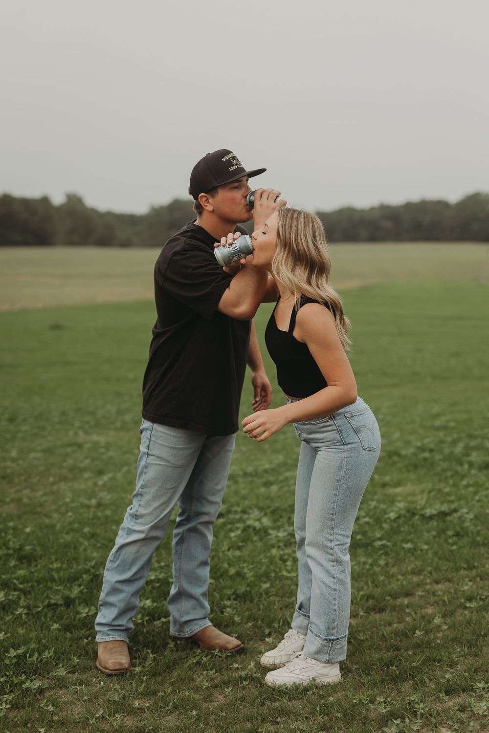 Two people playfully interact in a green field on a cloudy day wearing casual clothing.