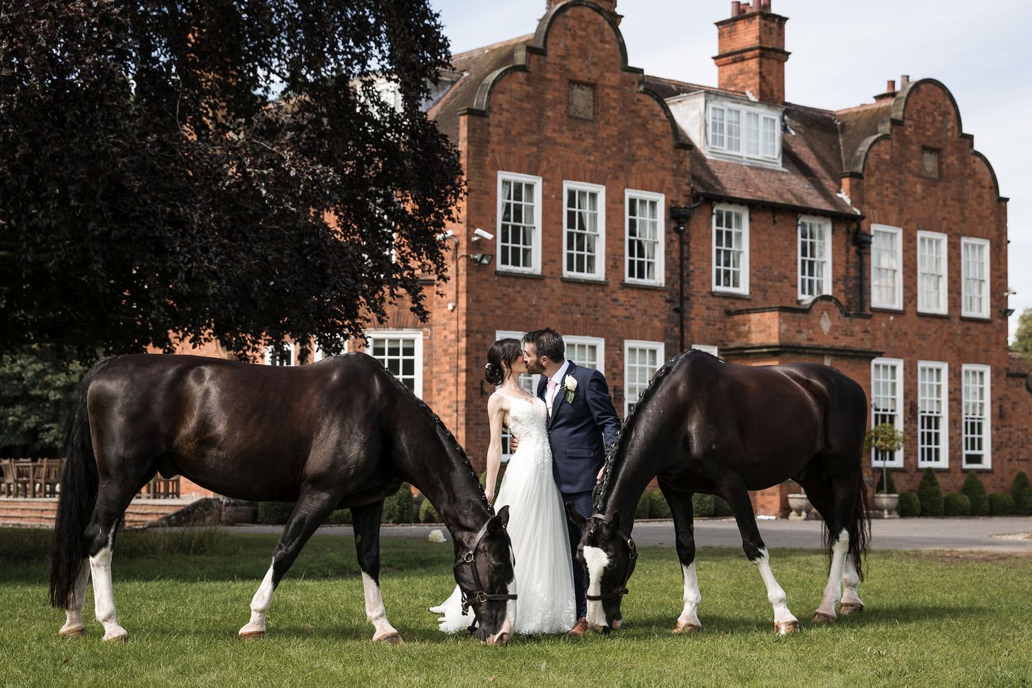 Bride and groom with two horses on the lawns in front of the red-brick Kelham House manor