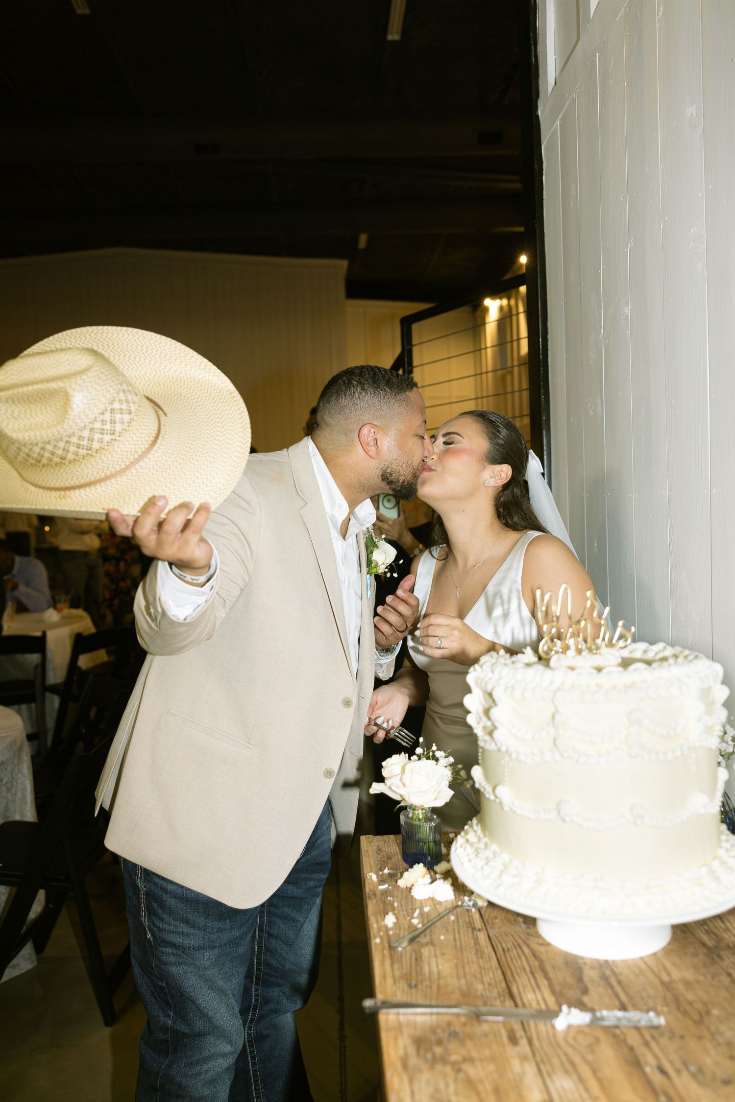 Couple sharing a romantic kiss beside a long wooden table during a wedding celebration.