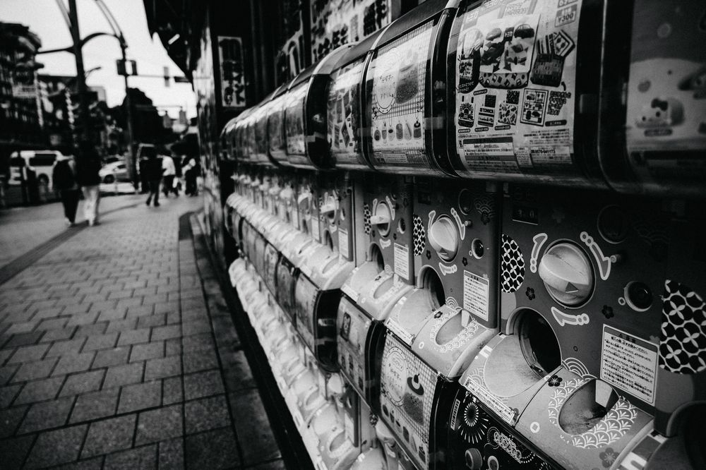 Street level view of storefronts with vending machines at night in black and white.