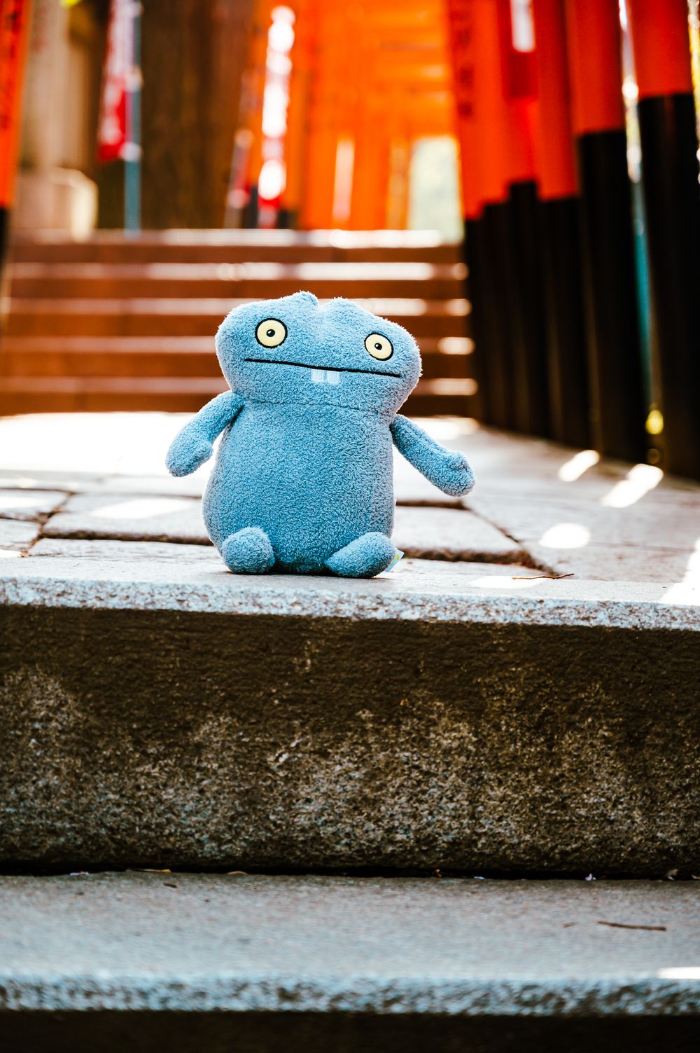 A blue plush toy sits alone on concrete steps in an urban setting.