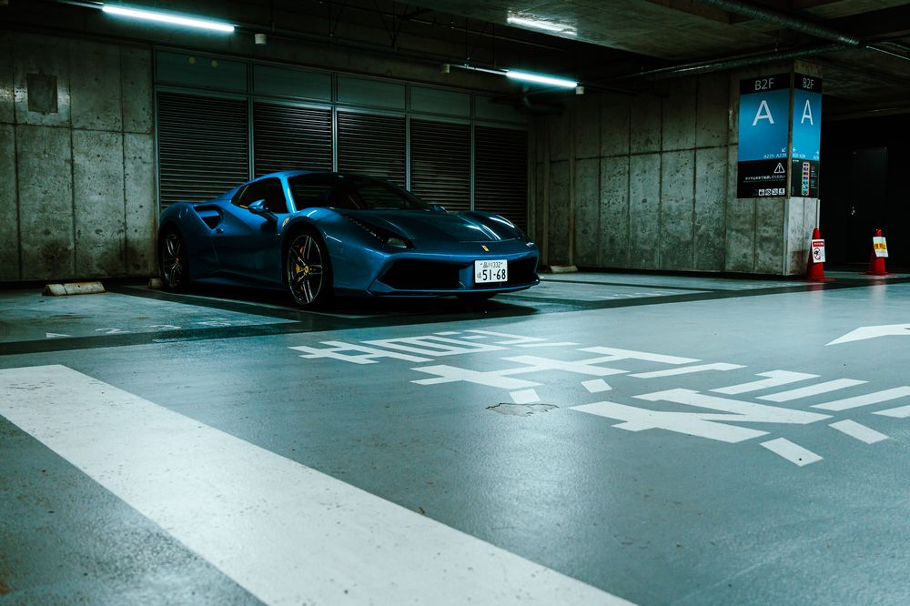Underground parking garage interior with marked spaces and fluorescent lighting illuminating concrete walls.