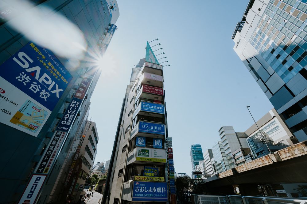 Bustling city street in downtown Tokyo with tall buildings and illuminated signs against a cloudy sky.