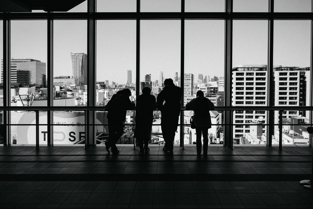 Silhouettes of people against large windows in an observation deck overlooking a city skyline.