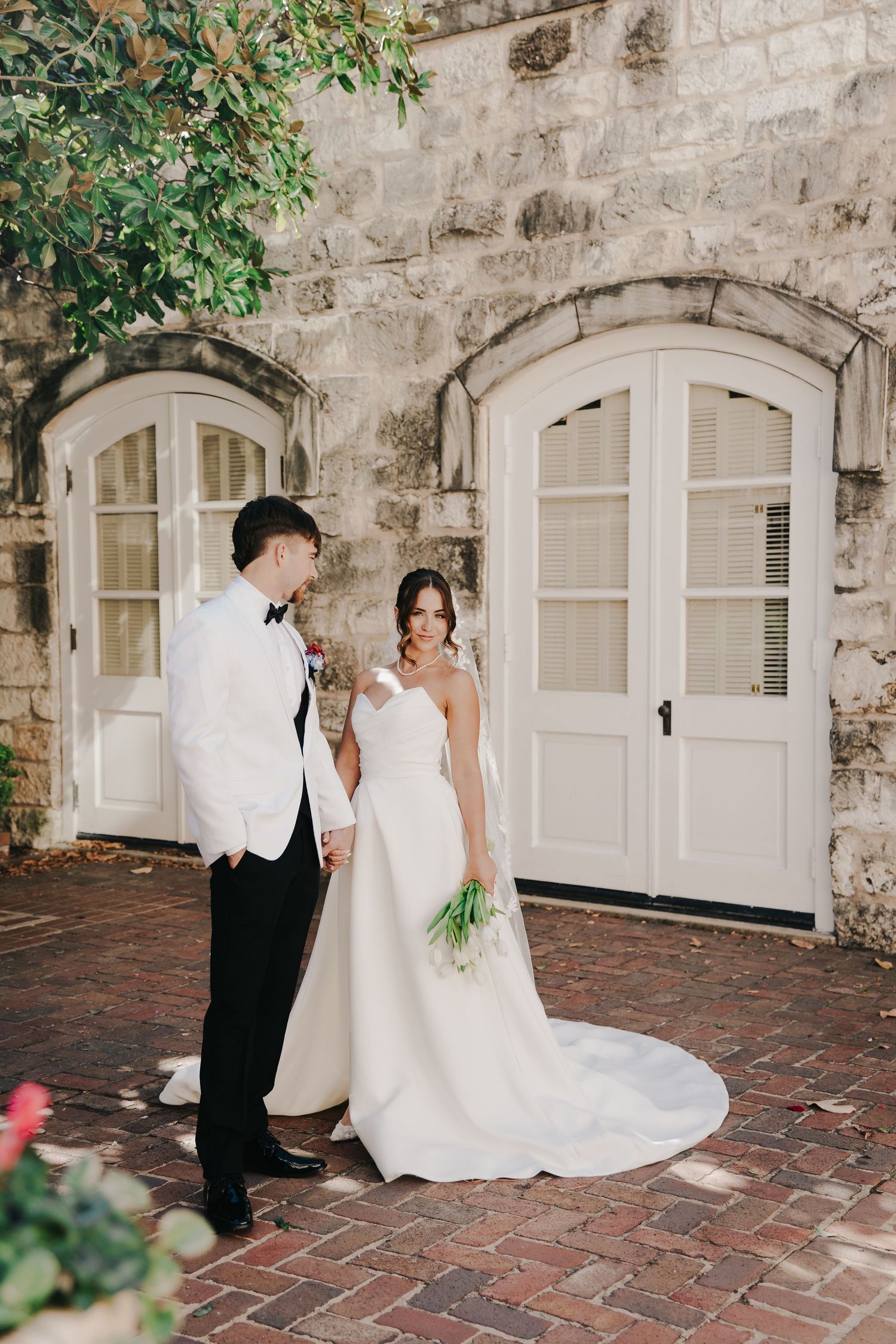 A couple in wedding attire shares romantic moments on a scenic stone balcony overlooking lush tropical vegetation.