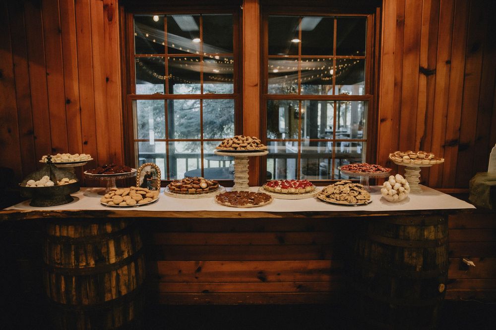 A rustic wooden dessert table features an array of pies and pastries displayed on tiered stands with mountain views through windows.