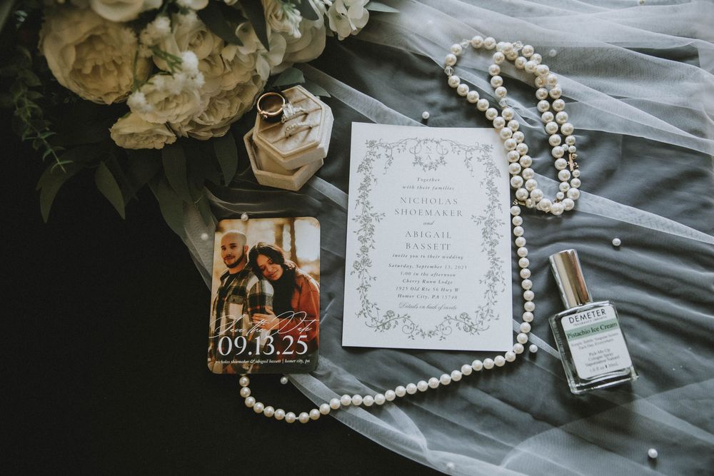 Flat lay of pearl necklaces, vintage wedding invitations, and keepsake items arranged on grey fabric backdrop.