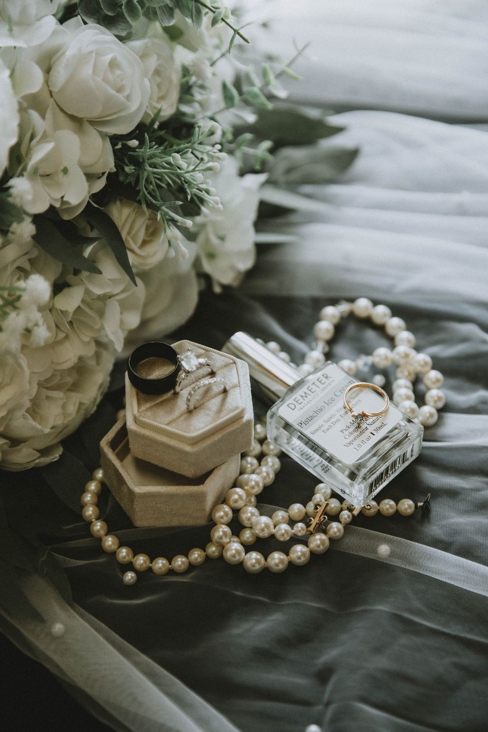 Pearl necklace and white wedding roses displayed with delicate styling elements on gray fabric background.