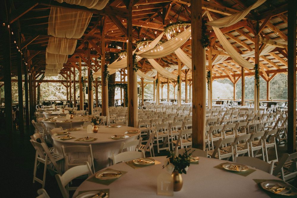Rustic wooden barn venue set up for an elegant wedding reception with white chairs and tables under vaulted ceilings.