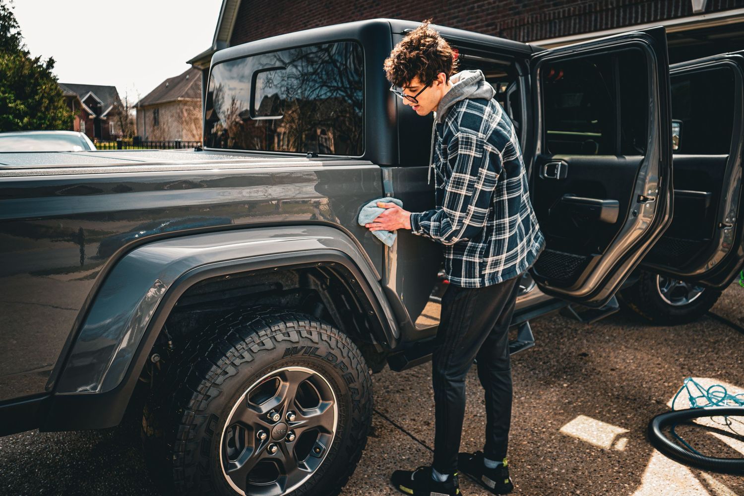 A person in a plaid shirt working on detailing the chrome wheel of a classic car parked outside in the rain.