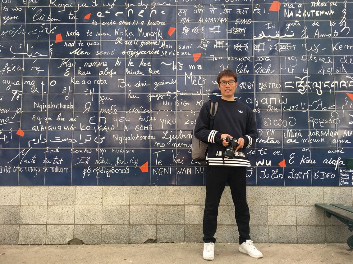 A tourist stands in front of the Wall of Love in Paris with its iconic blue wall covered in handwritten love declarations.