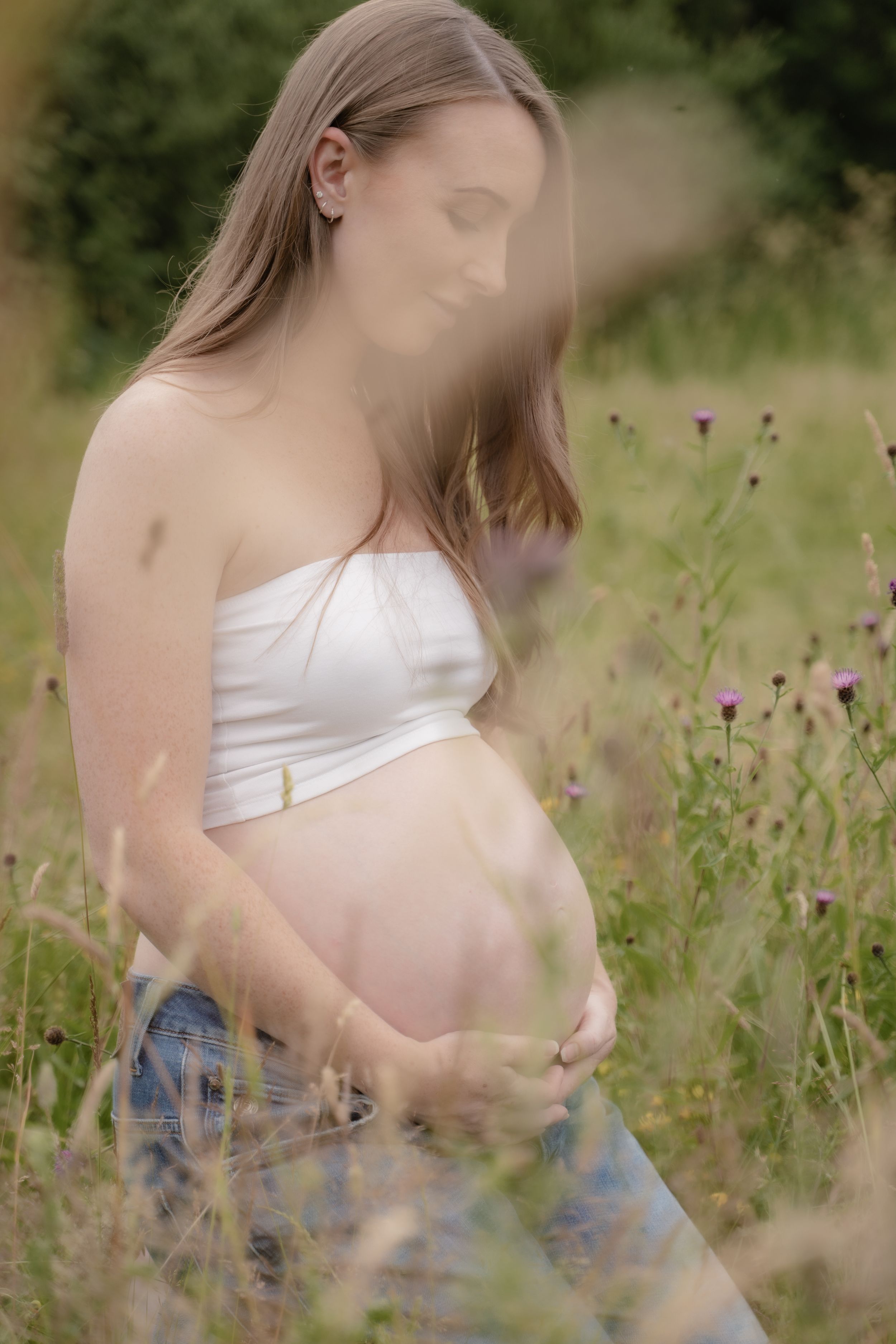A maternity photo sequence showing a pregnant woman in a white top and jeans standing in a wildflower meadow.