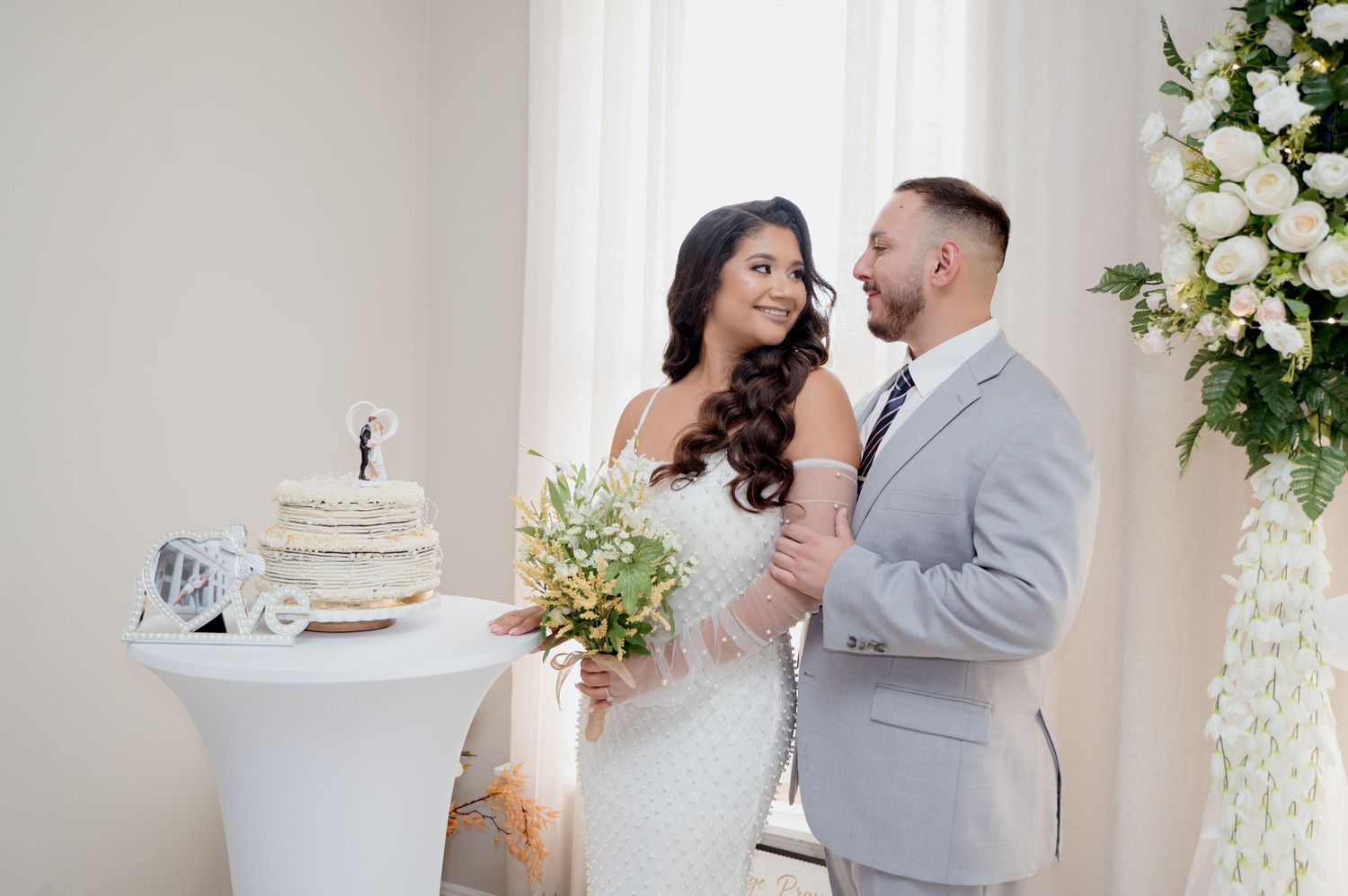 A romantic wedding couple shares intimate moments while cutting cake and dancing in an elegant white reception venue.
