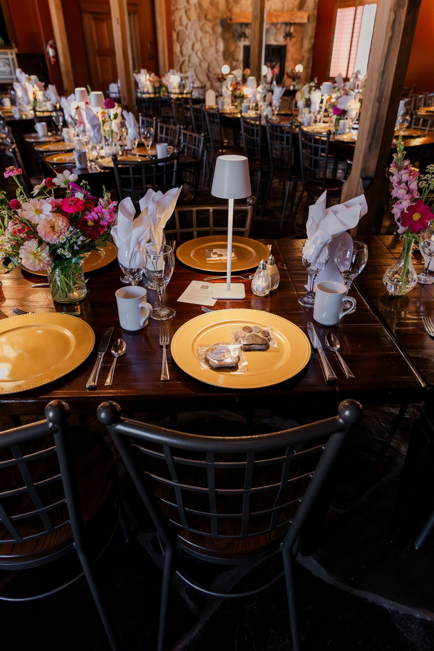 Formal table setting with gold charger plates and white napkins in a rustic stone-walled dining room at Hauser Hall in Kitchener, Ontario.