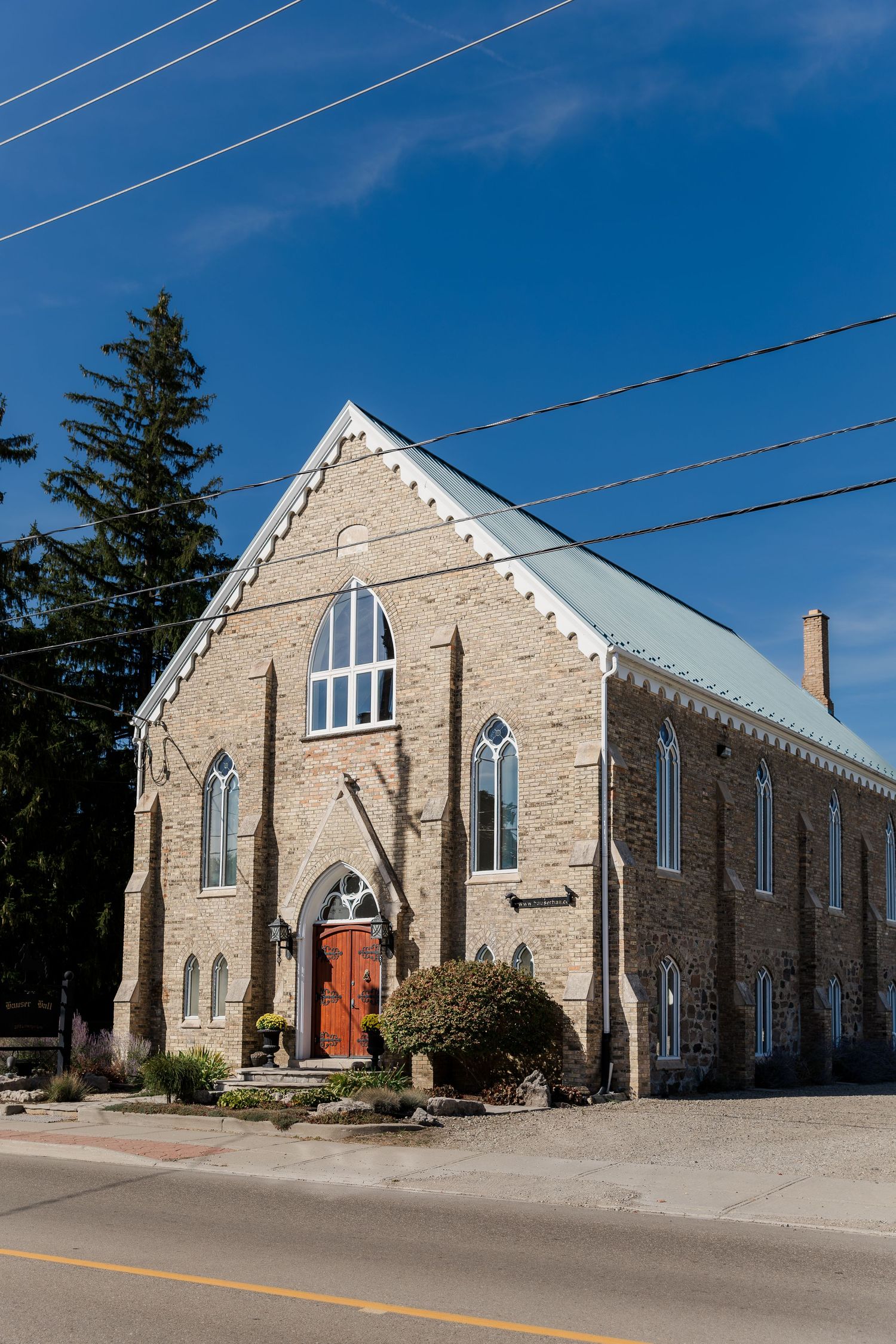 Stone church exterior with Gothic windows and red door against bright blue sky on sunny day Hauser Hall in Kitchener, Ontario.