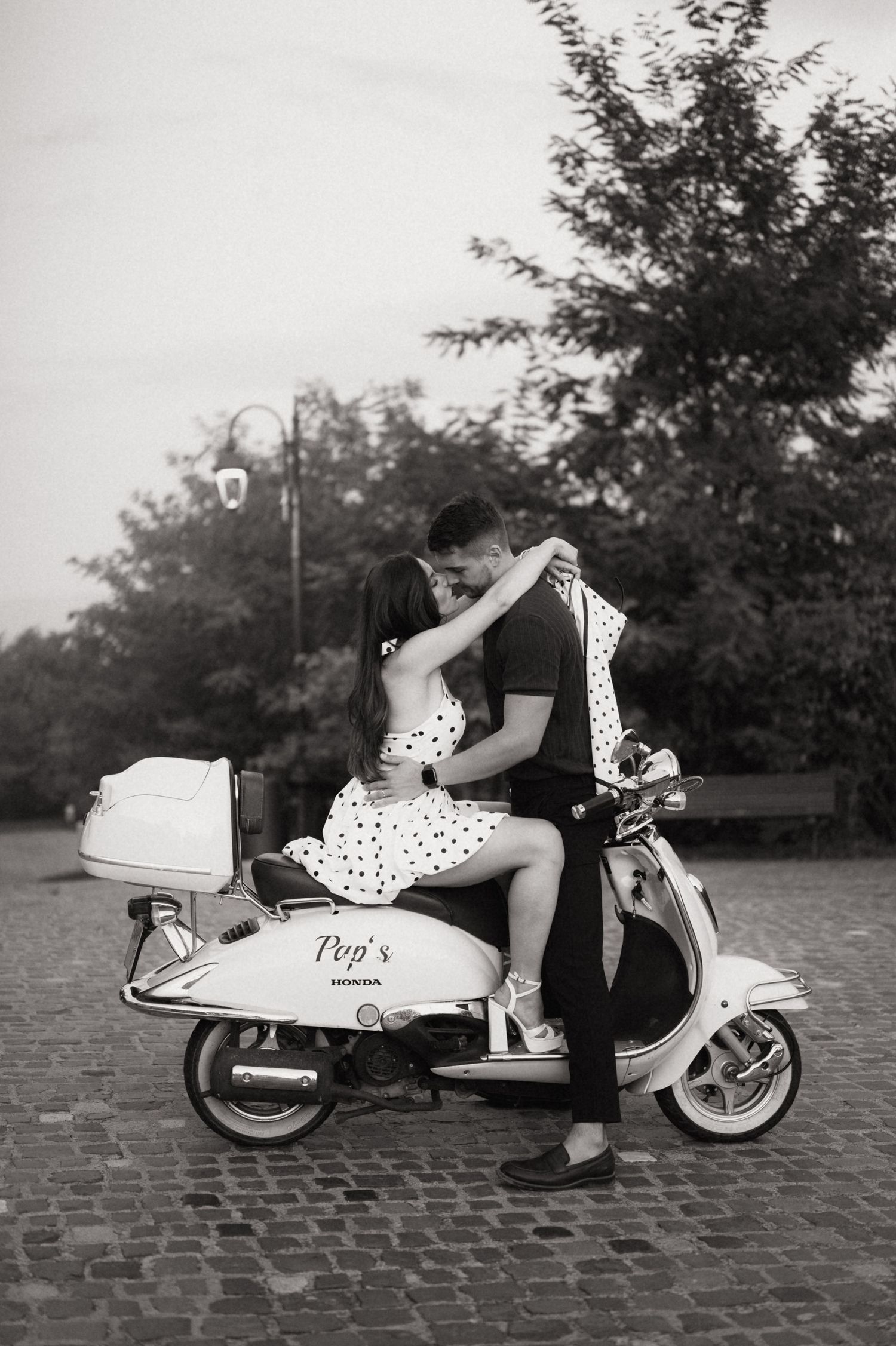 A sequence of black and white photos showing a vintage motor scooter on cobblestone pavement from different angles.