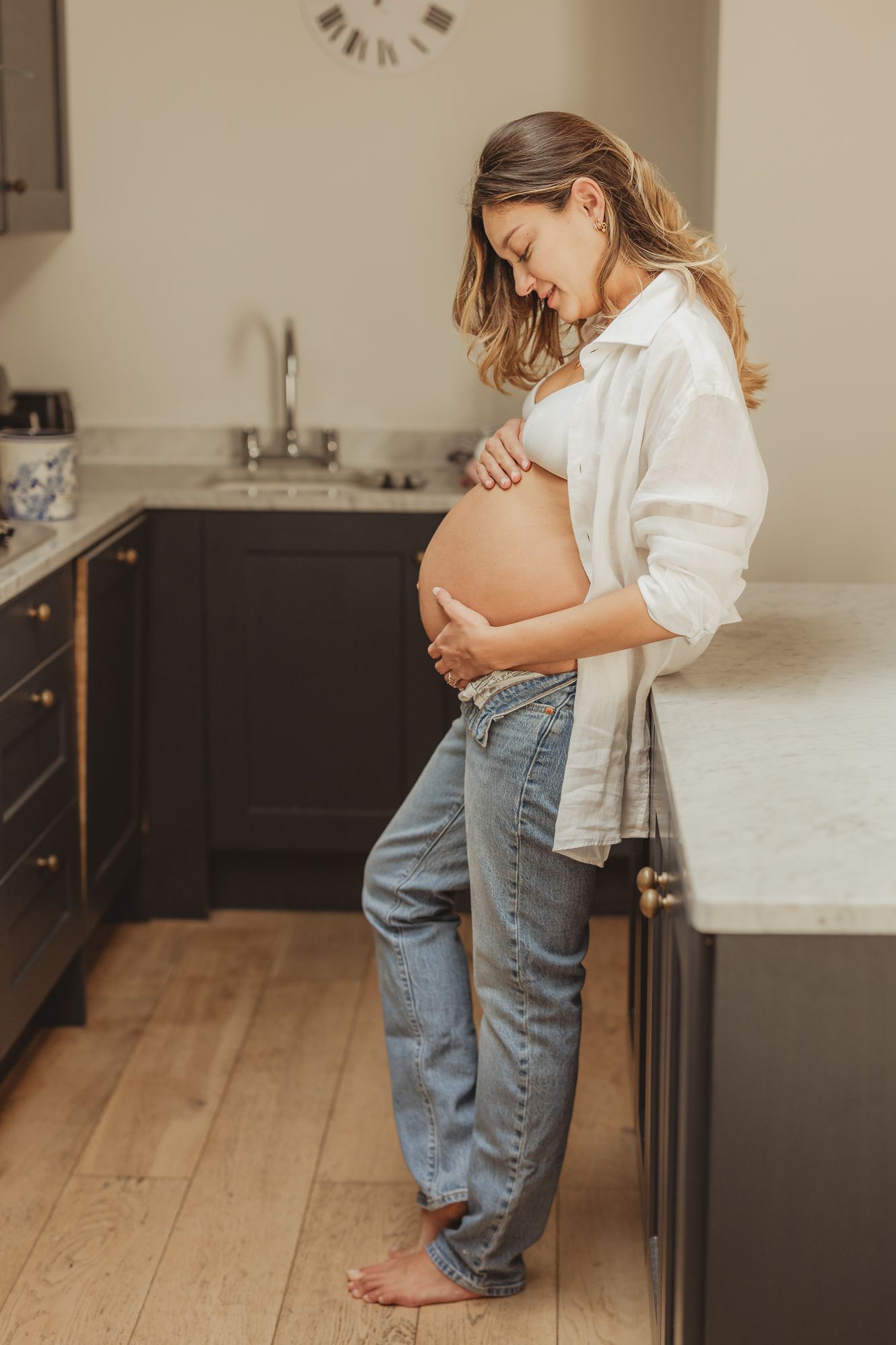 Maternity photoshoot in a modern kitchen with white countertops and wooden floors.