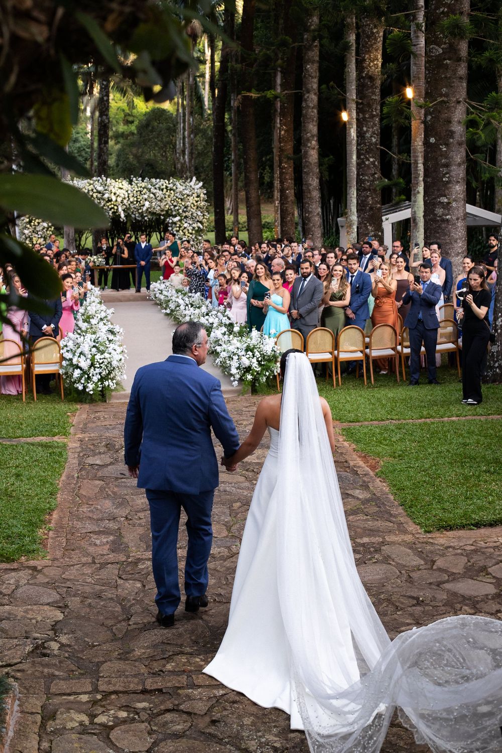Couple walking down stone pathway after ceremony as guests watch in wooded outdoor setting.