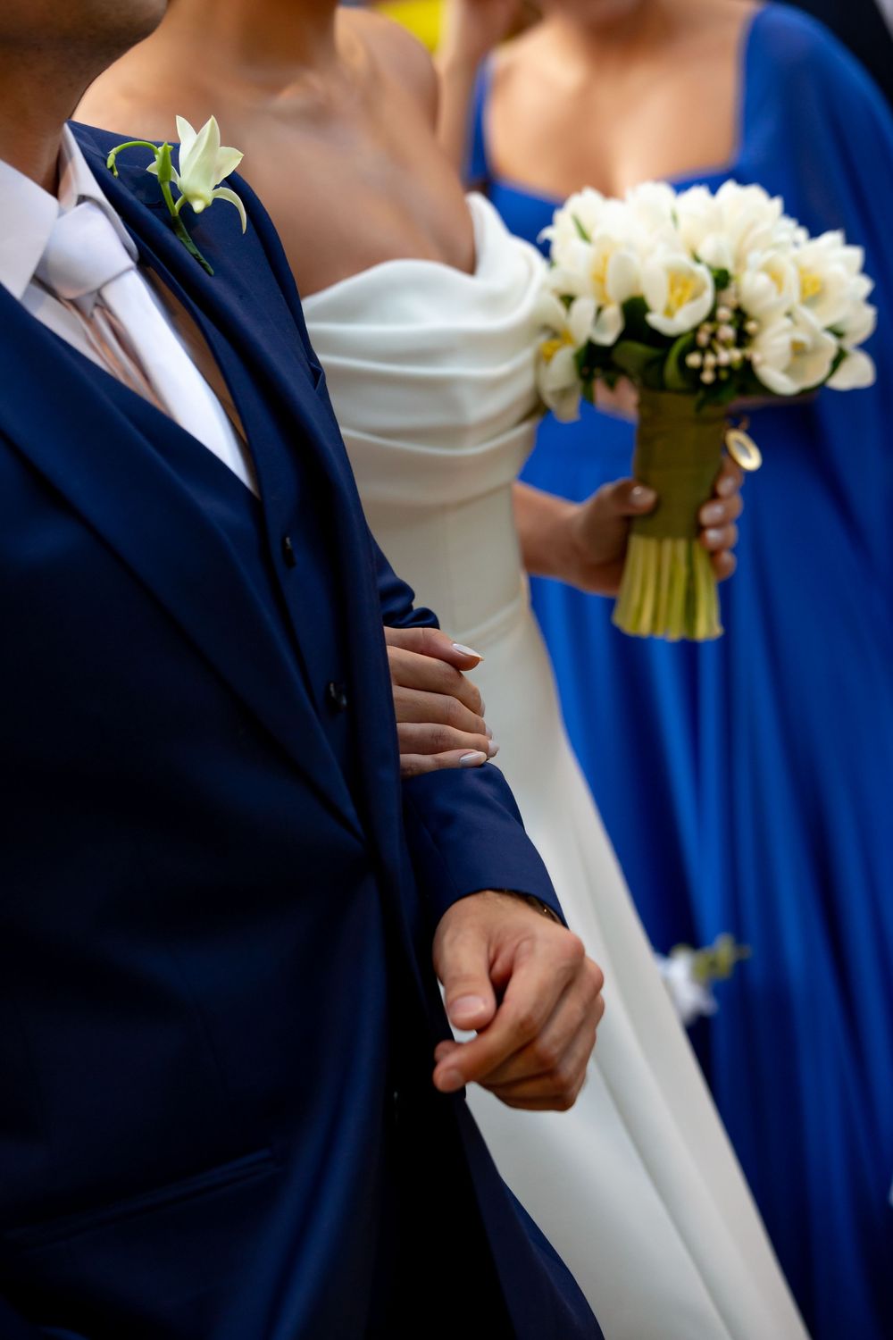 Wedding party members in navy blue suits and a white dress gathered together with floral bouquets.