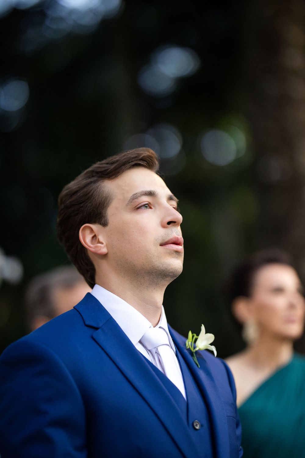 Candid moment of a person in a navy suit looking upward with emotion during an outdoor ceremony.