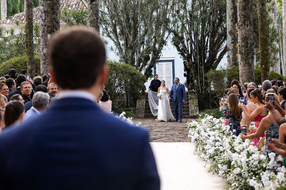 Outdoor wedding ceremony setting with white floral arrangements lining a pathway between tall trees.