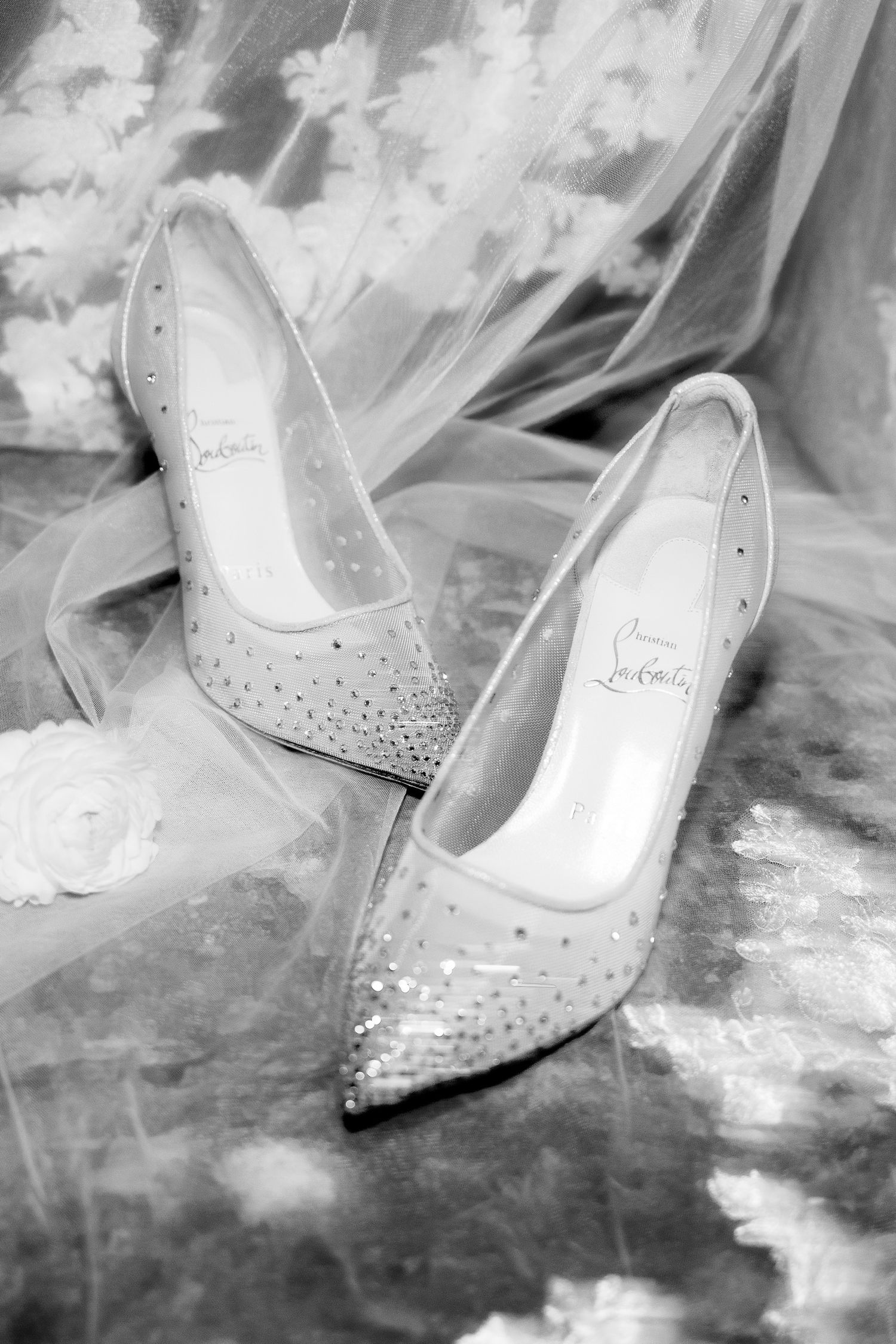 Black and white photo of crystal-embellished Christian Louboutin bridal heels on lace veil.