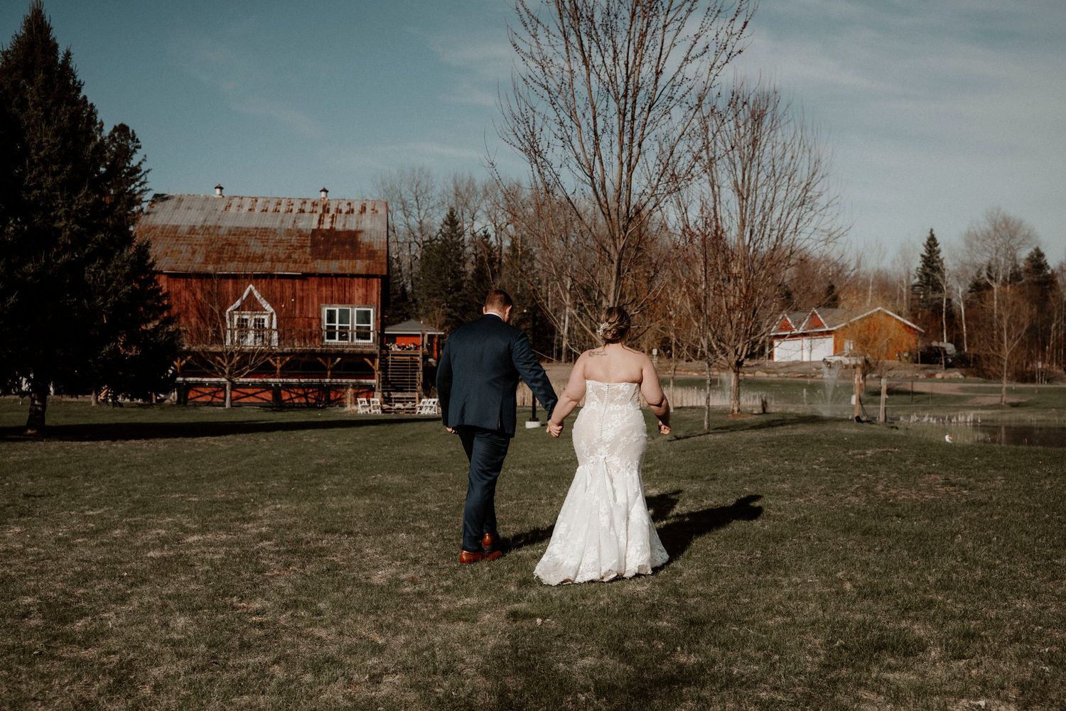 Wedding scene in a rustic outdoor setting with red farmhouse buildings and open fields.Bride and groom at rustic barn wedding venue Muskoka