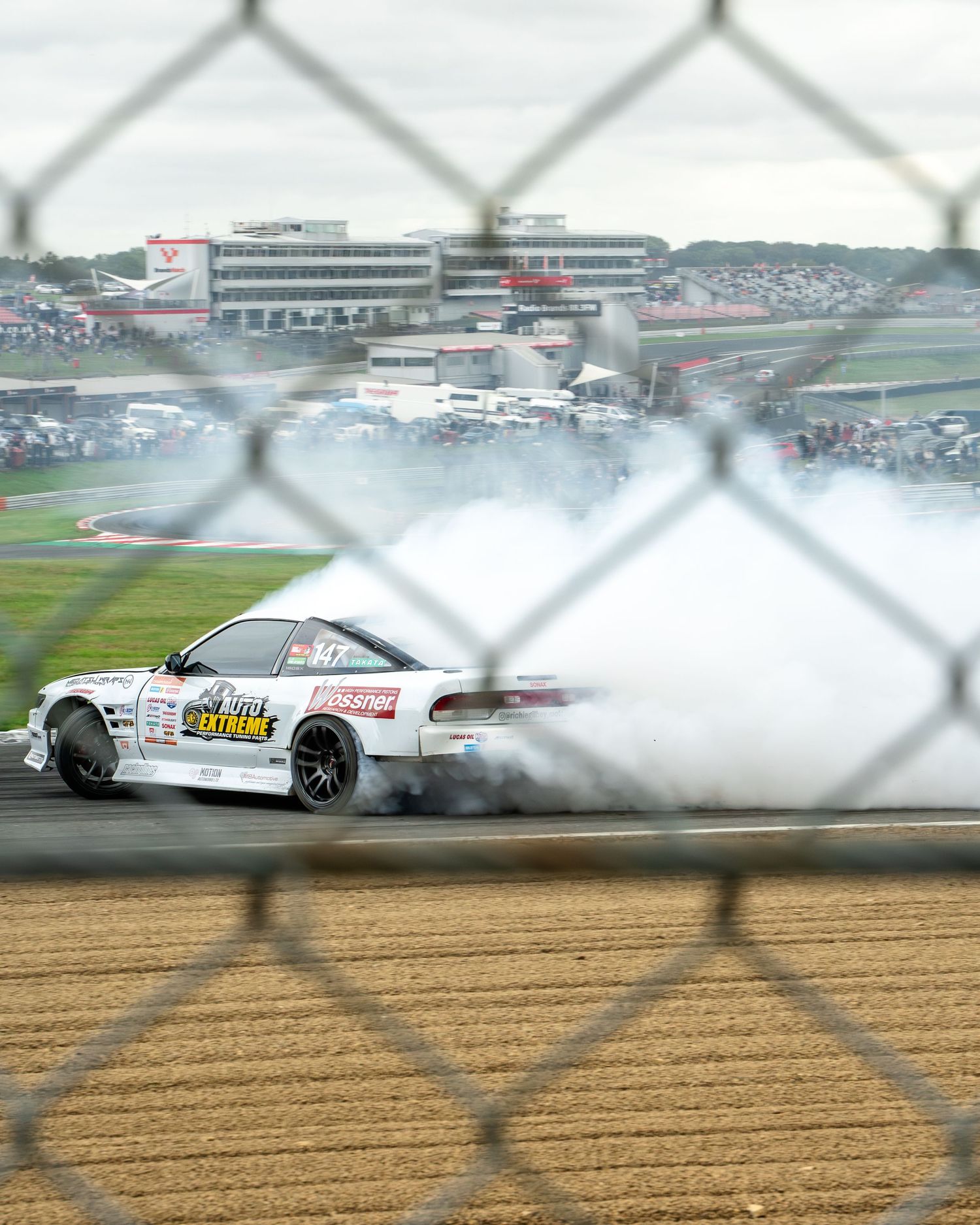 White race car drifting and creating smoke on a racing circuit.
