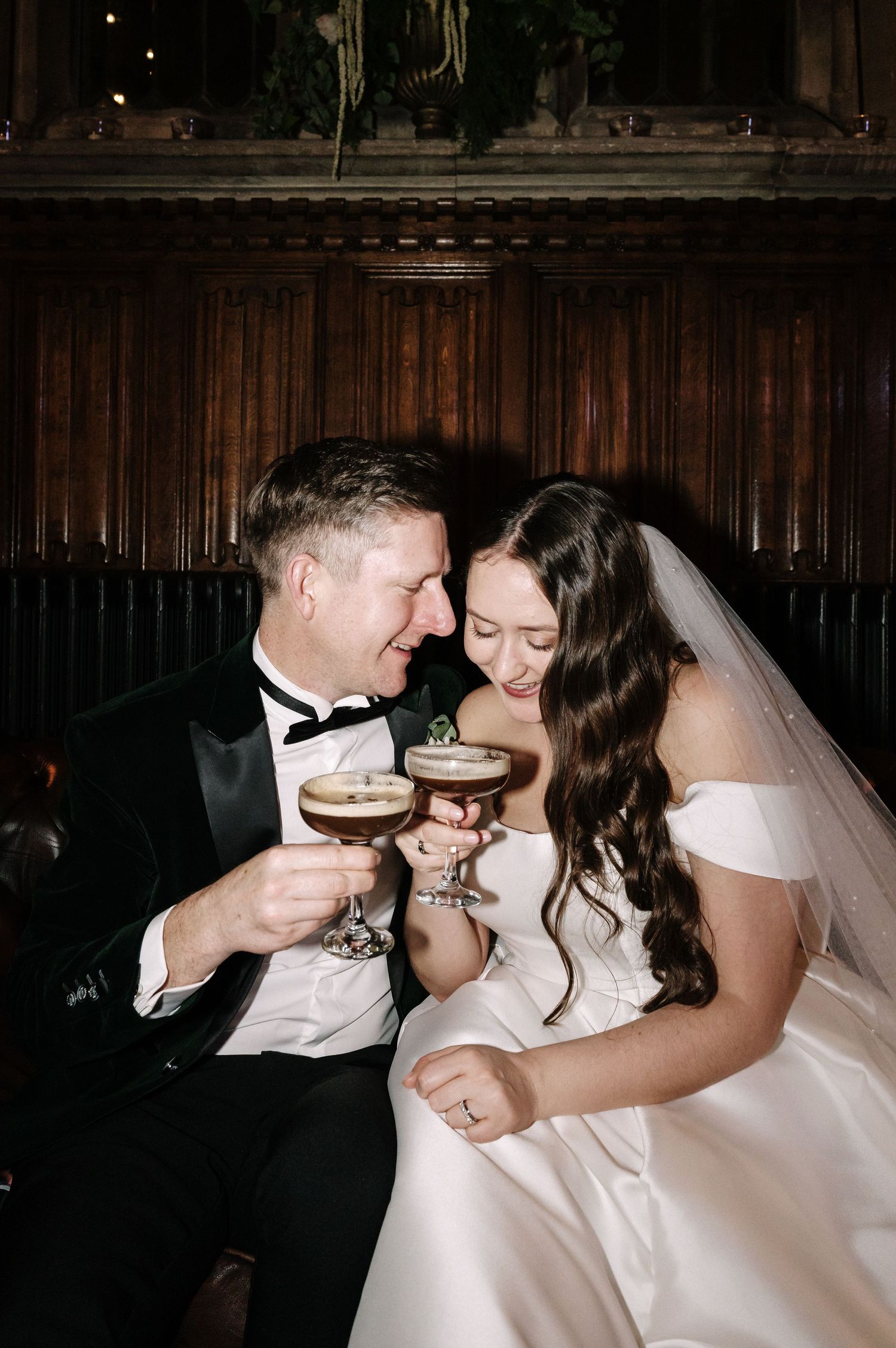A newlywed couple shares an intimate moment while sipping champagne at their wedding reception in a wood-paneled venue.
