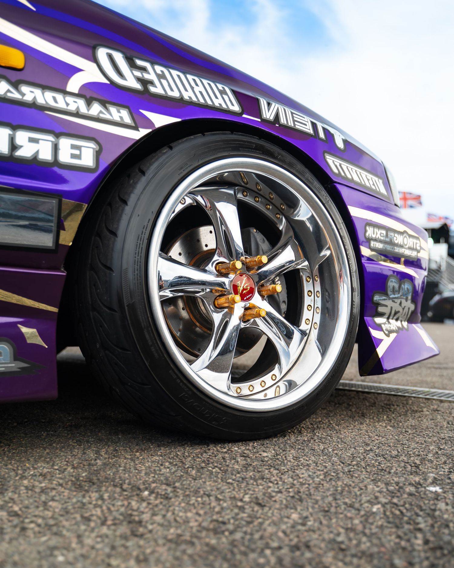 Custom chrome wheels with purple car body visible on a gravel surface.