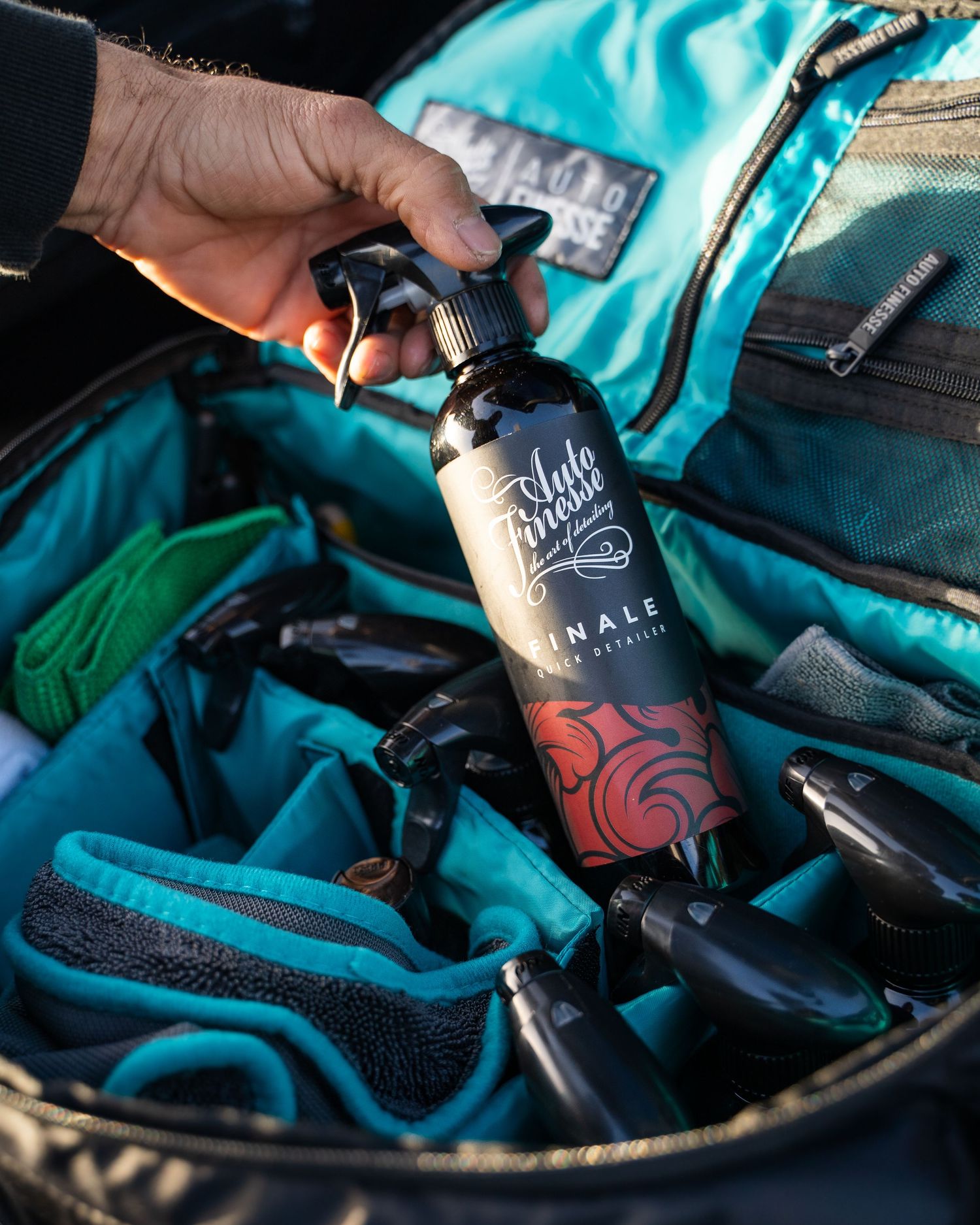 Auto detailing spray bottle shown against turquoise car care equipment bag.
