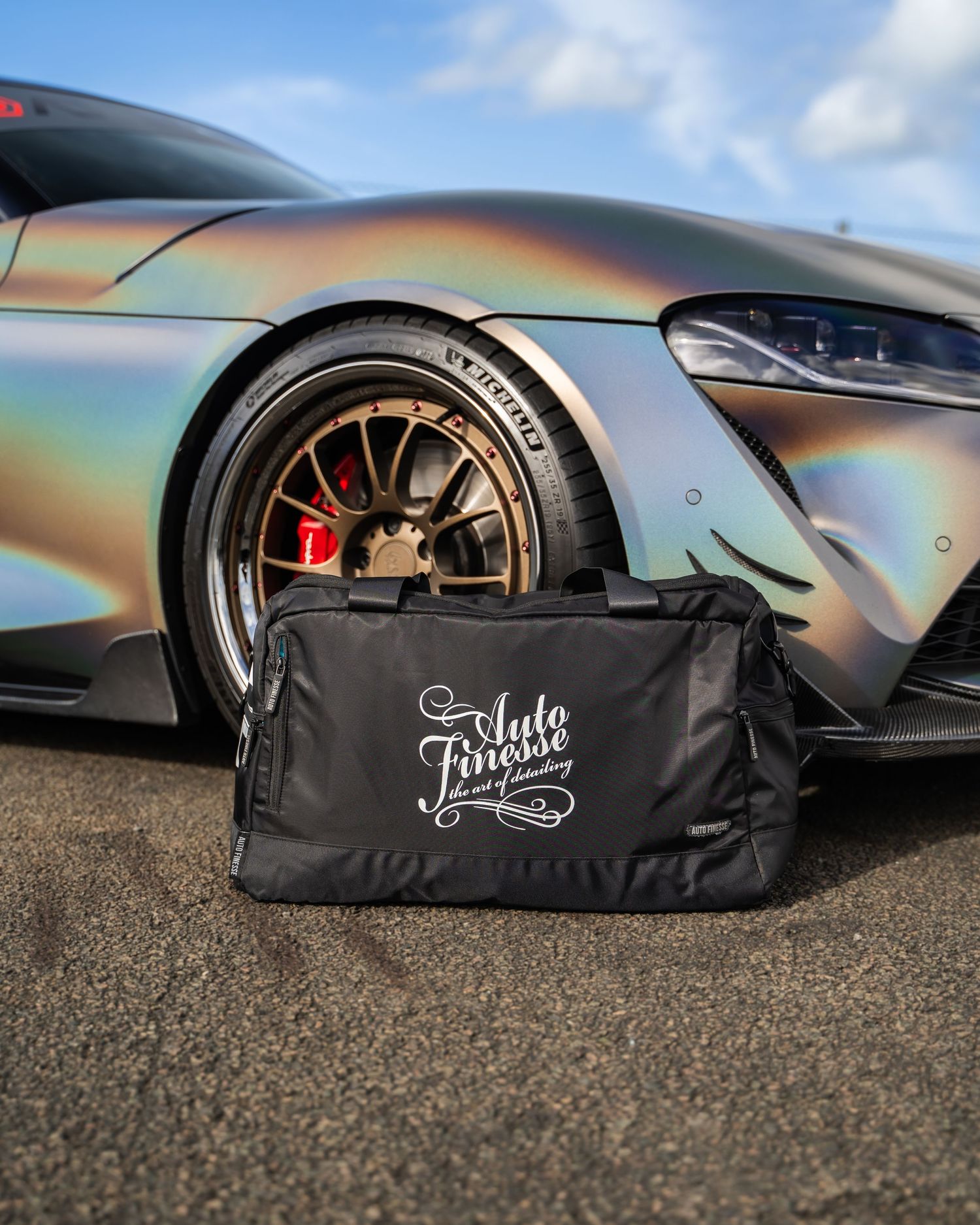 Close-up of iridescent Toyota Supra wheel with black detailing bag in foreground.