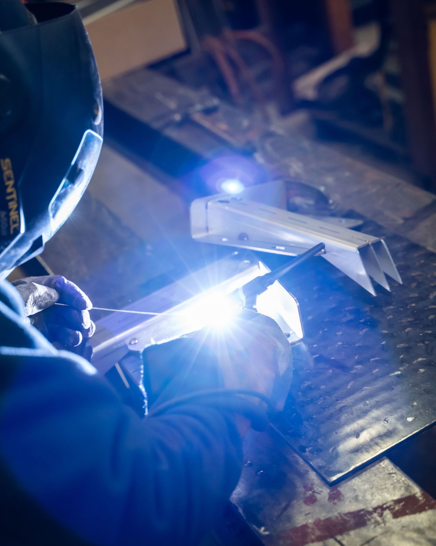 Bright blue welding sparks illuminating a metal workpiece during fabrication.