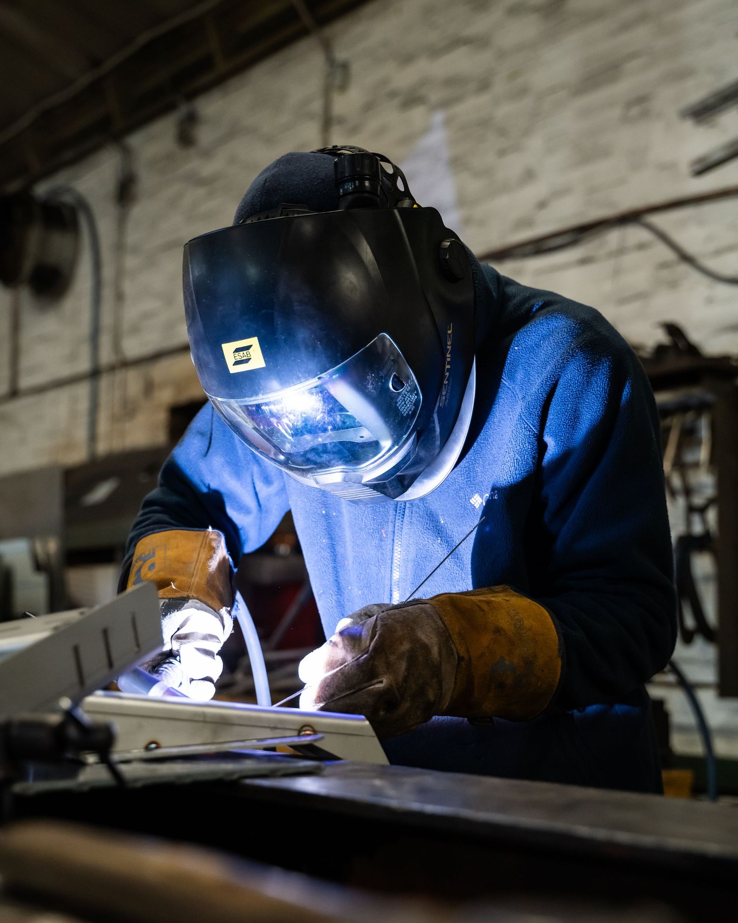 Welder working on metal components in a workshop with bright blue welding light.