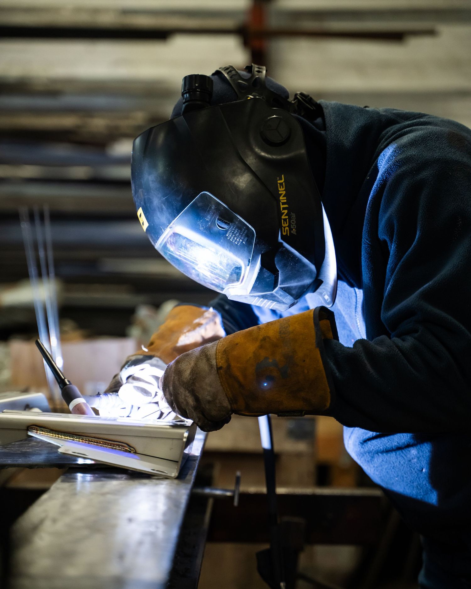 Professional welder in protective gear performing precision welding on metal parts.