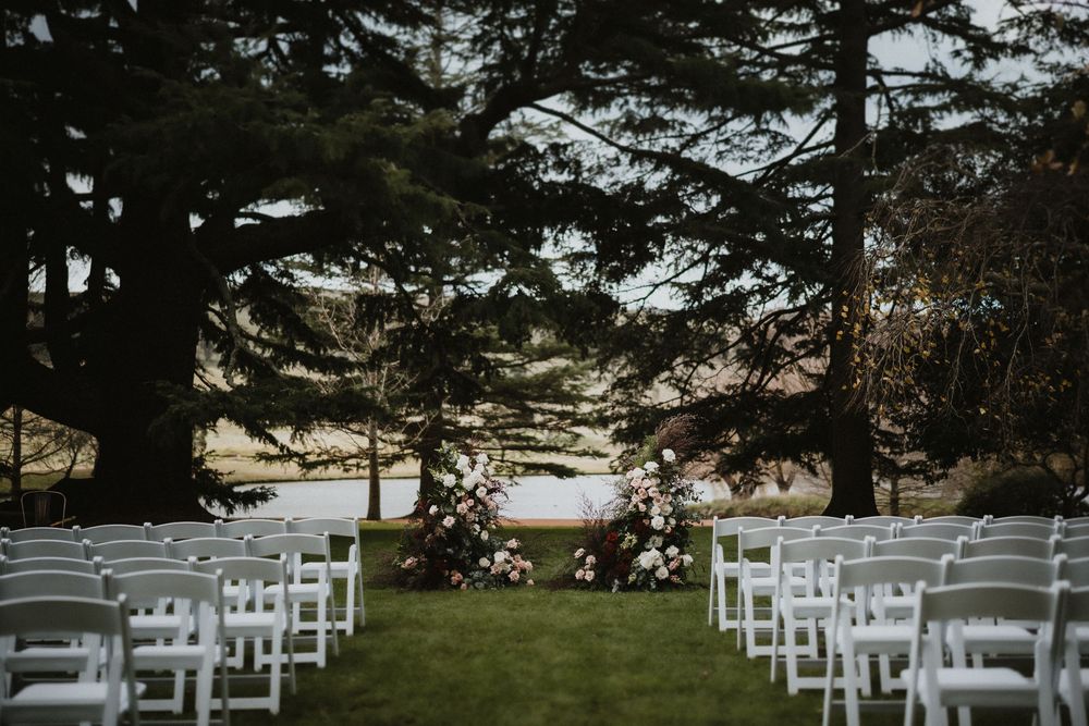 Rows of white chairs set up for an outdoor ceremony under tall pine trees.