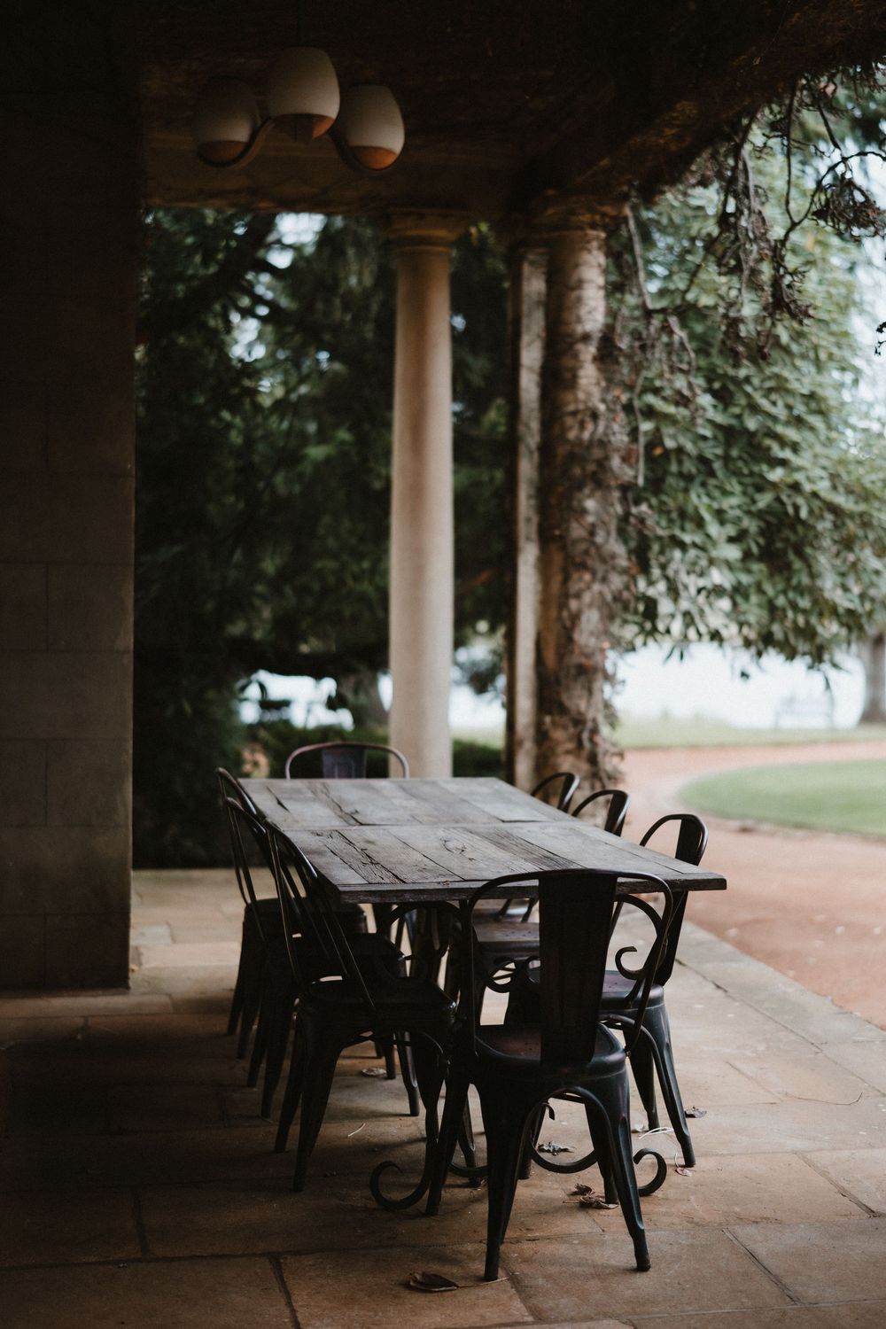 Rustic wooden dining table with black chairs under a covered patio area.