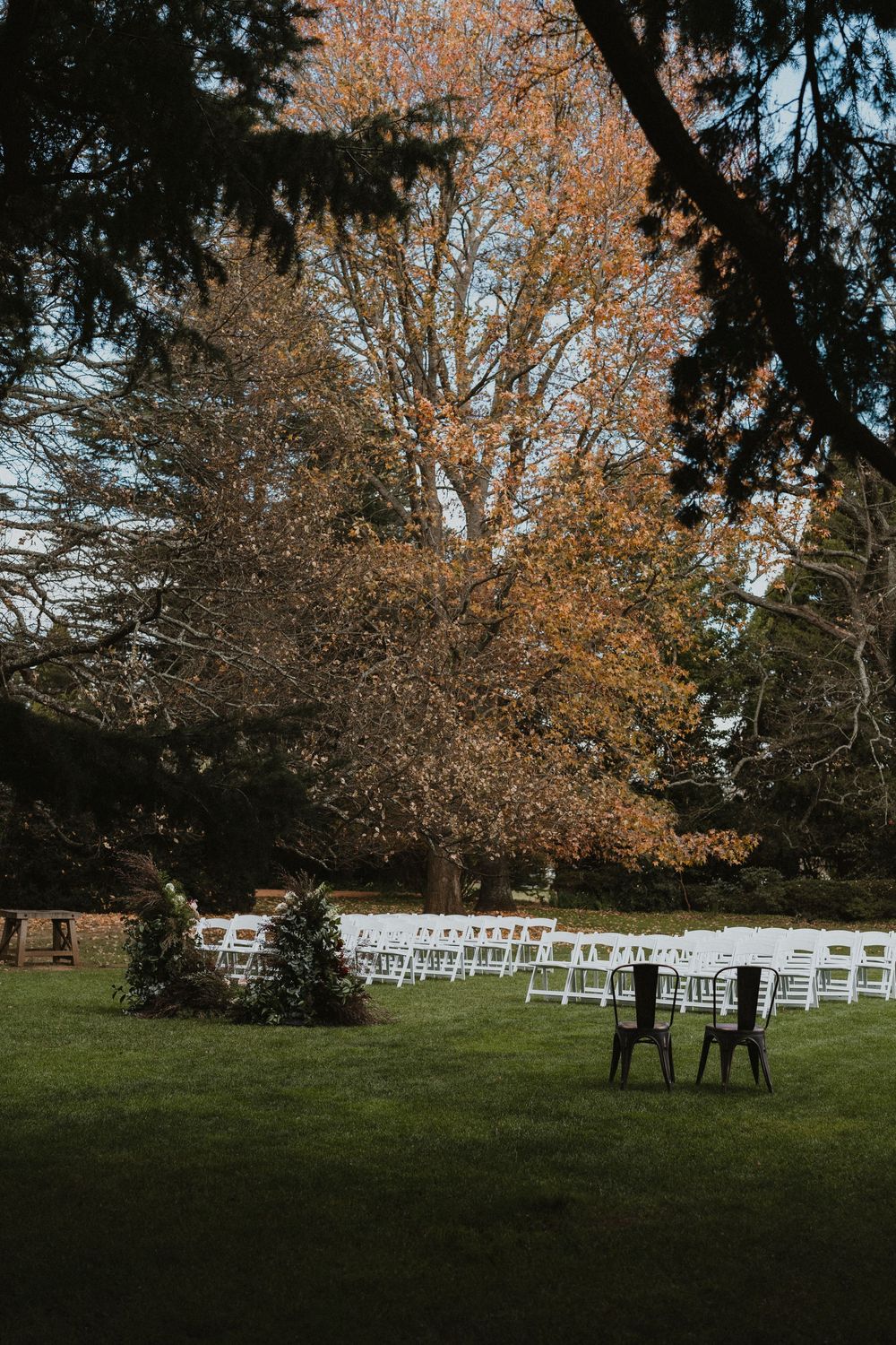 Outdoor wedding ceremony setup with white chairs and trees displaying autumn colors.