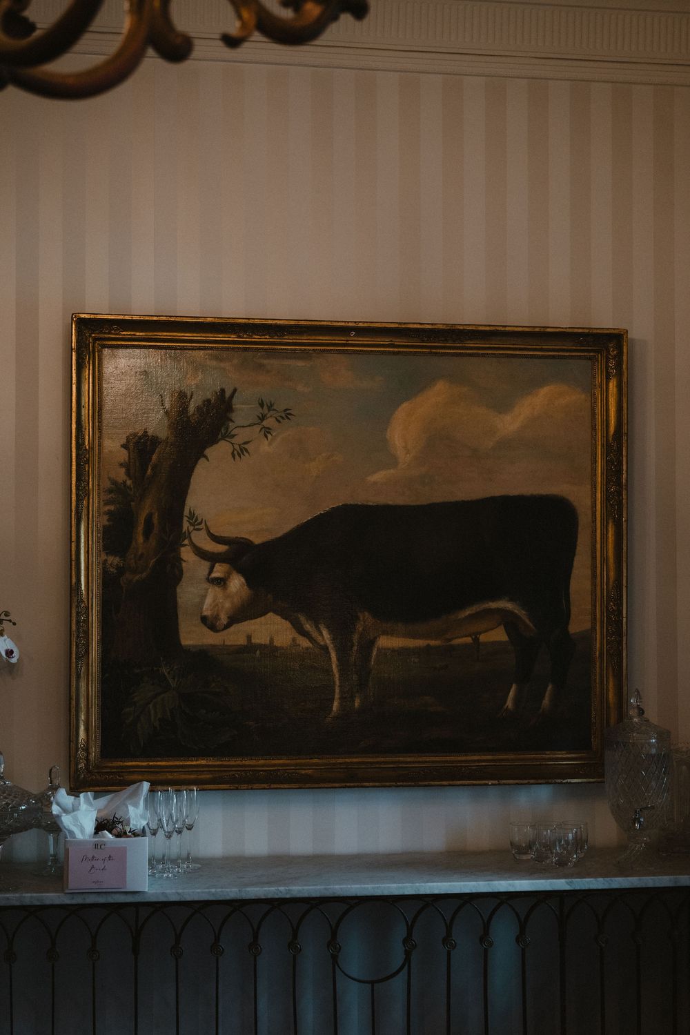 Vintage landscape paintings in ornate gold frames hanging on a striped wallpapered wall.