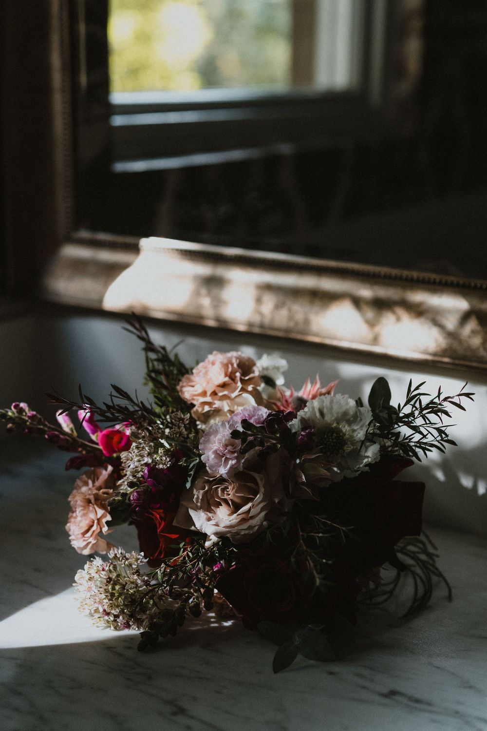 Delicate floral arrangement with pink and purple blooms sitting in natural window light.