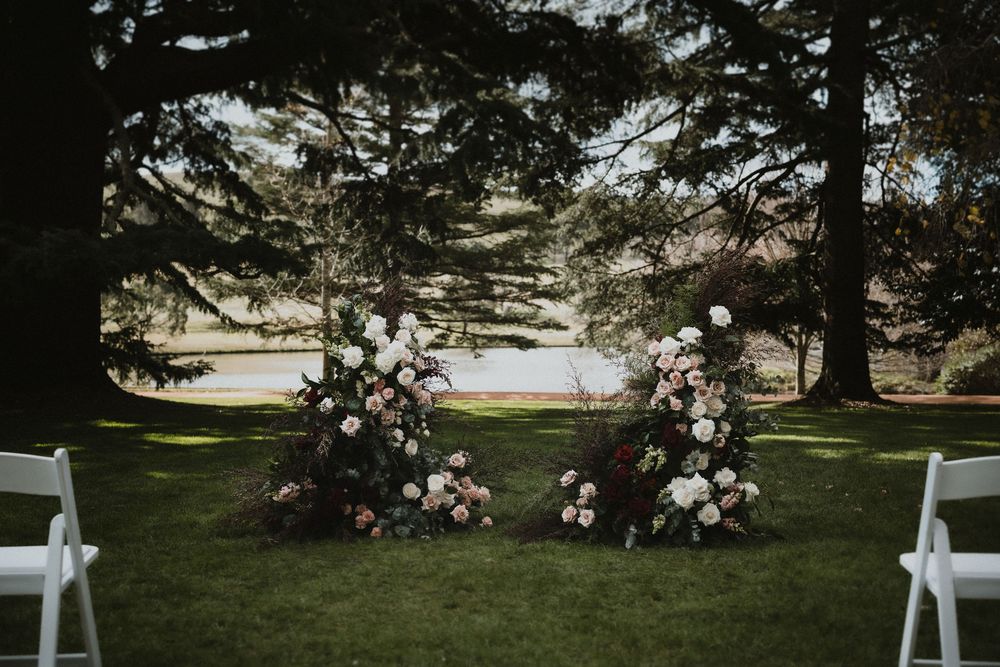 White chairs arranged on a lawn for an outdoor ceremony with evergreen trees in the background.