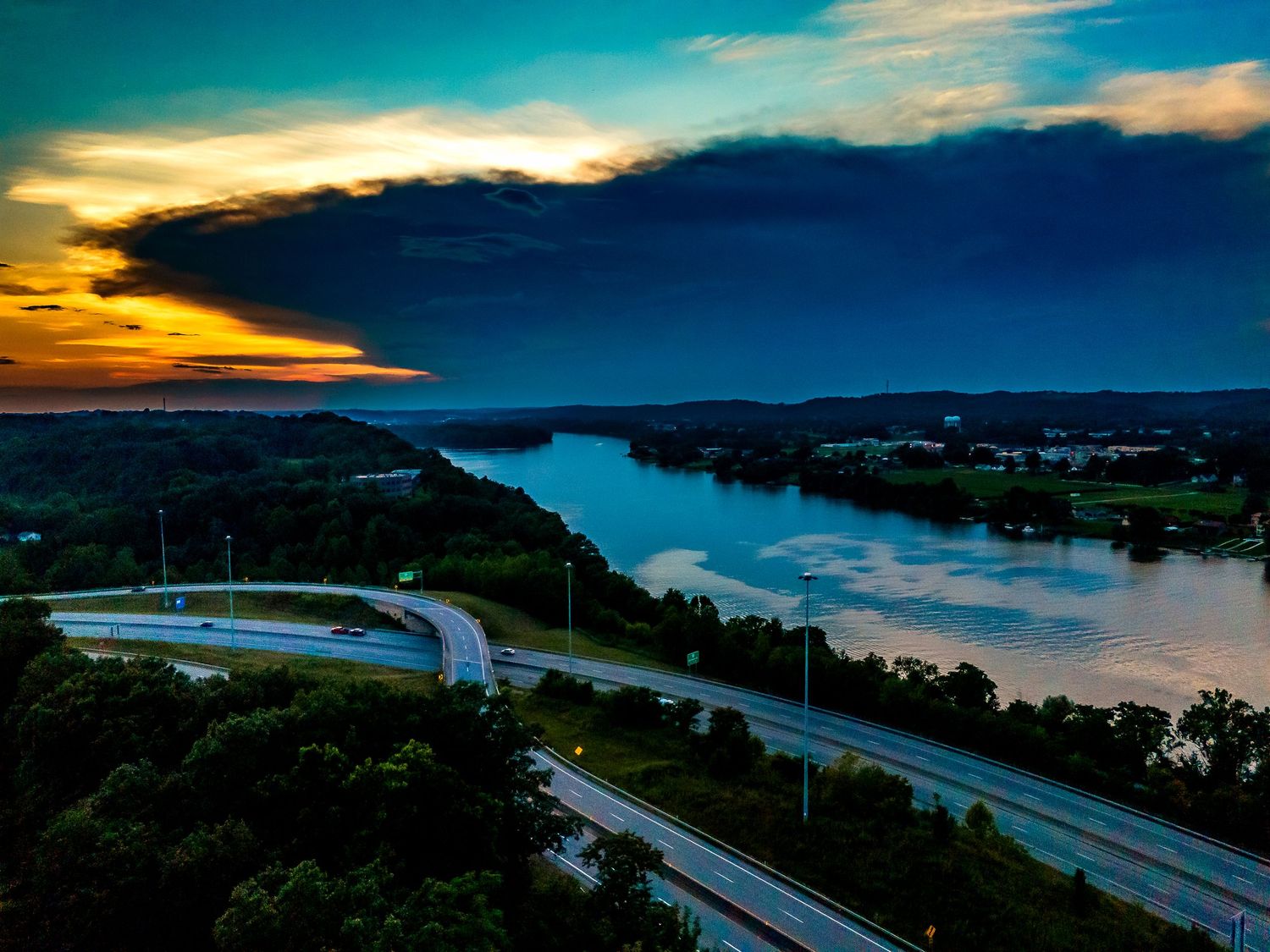 Beautiful aerial view of a winding highway along a scenic lake at sunset with dramatic clouds in the sky.