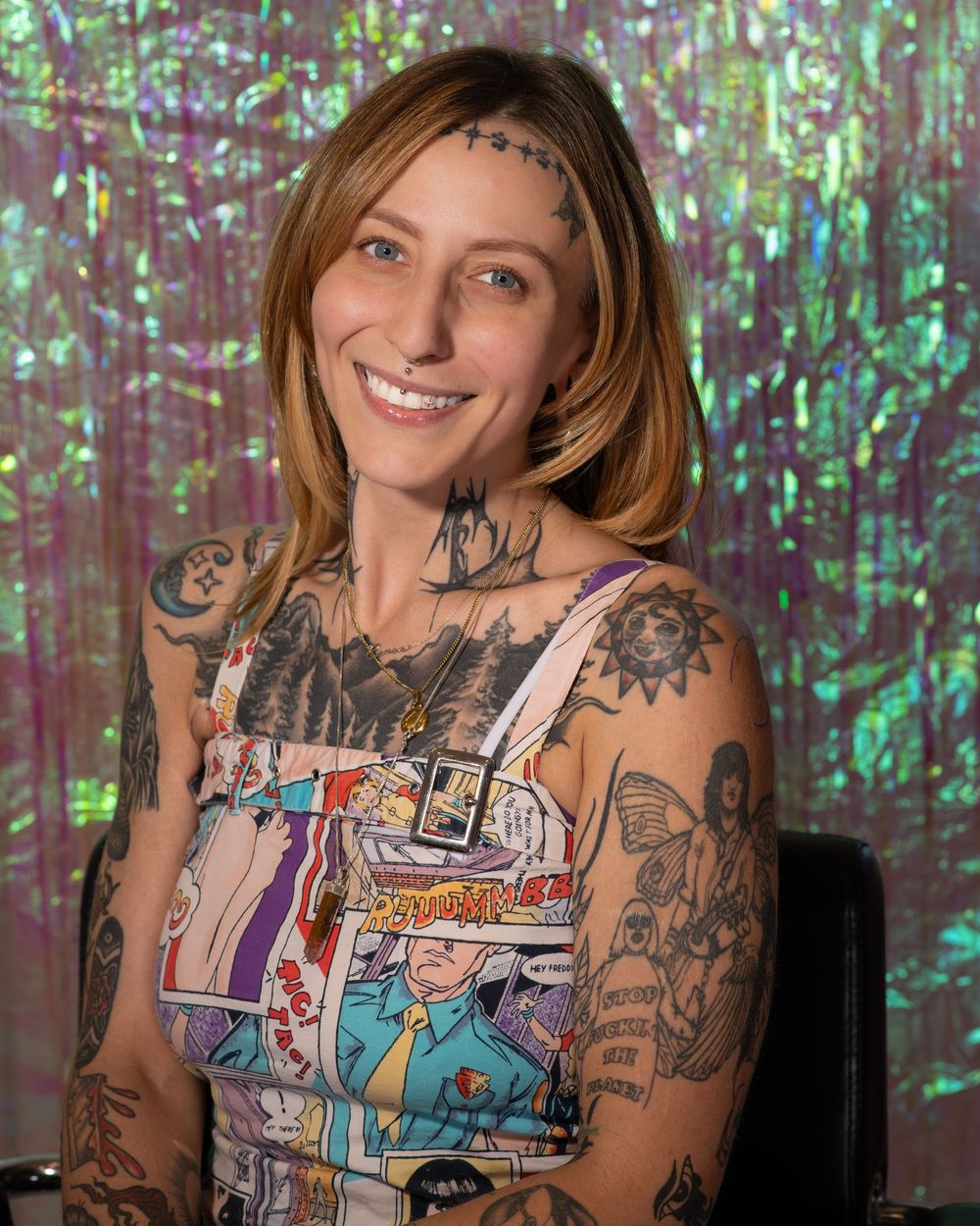 Tattooed woman smiling in comic book print dress against a shimmering iridescent green backdrop.