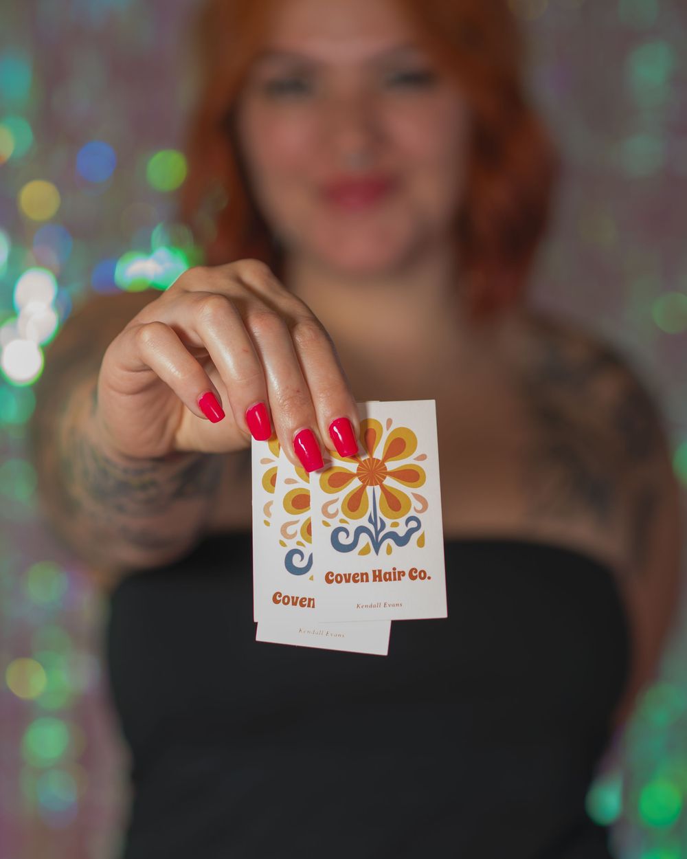 Woman with red nails holding a Coven Hair Co. business card toward the camera in soft focus.